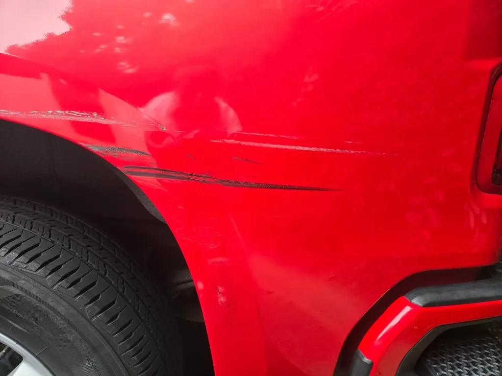 Deep crease and paint transfer along the bedside of a red Chevrolet Silverado.