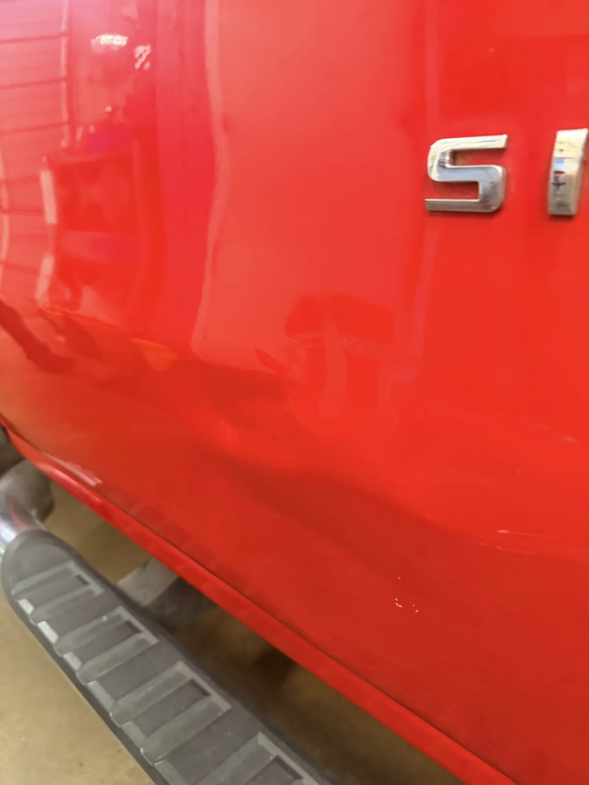Dent on the rear door of a red Chevrolet Silverado, below the badge.