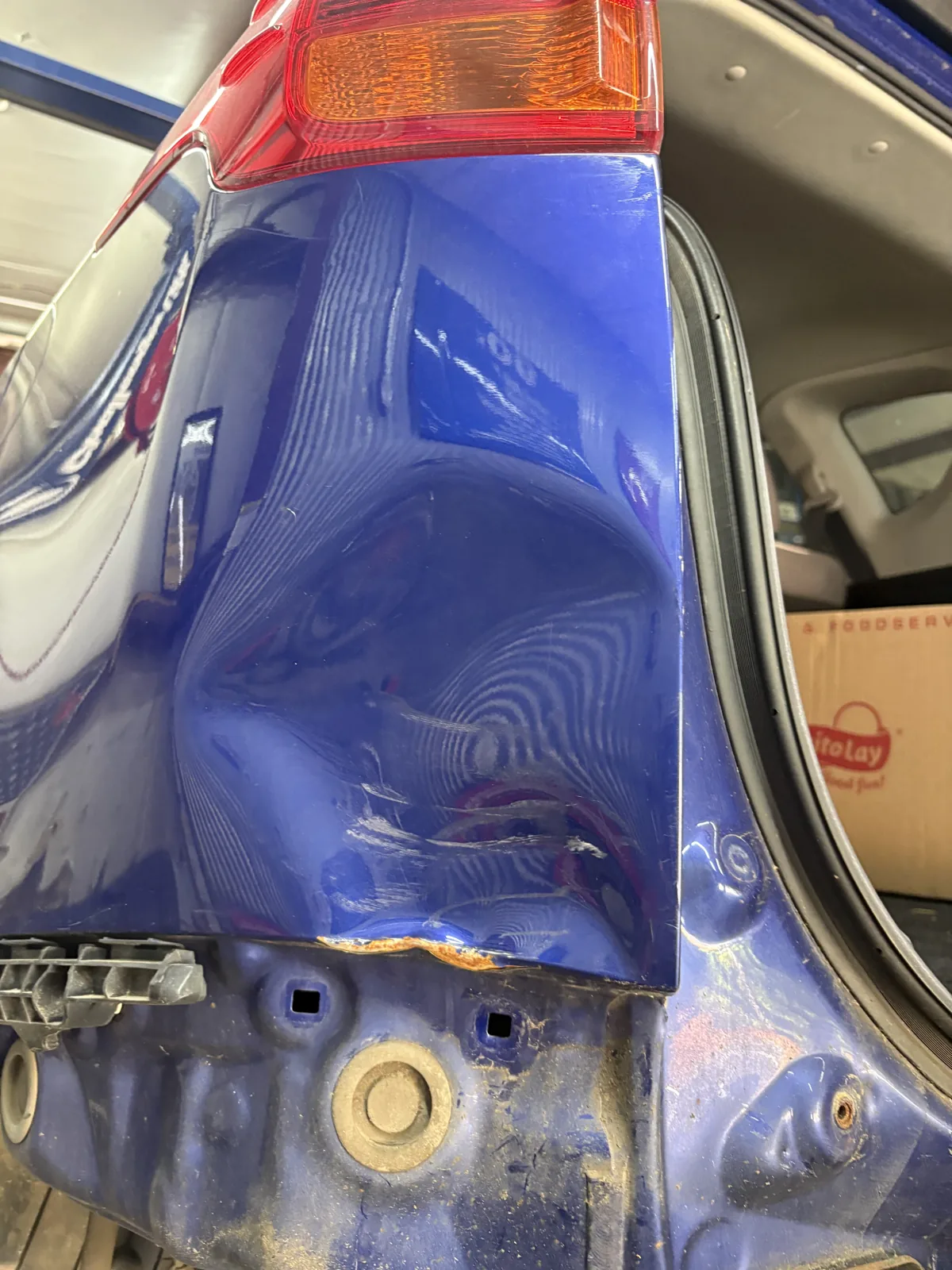 Severe crease folded into the rear quarter panel of a blue vehicle, beside the taillight.