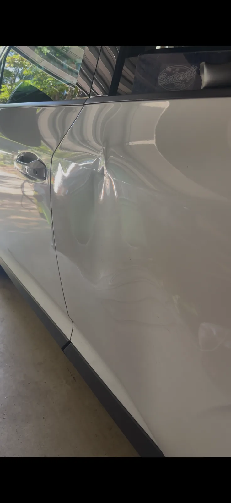 Long crease across the driver's door of a white SUV before repair.