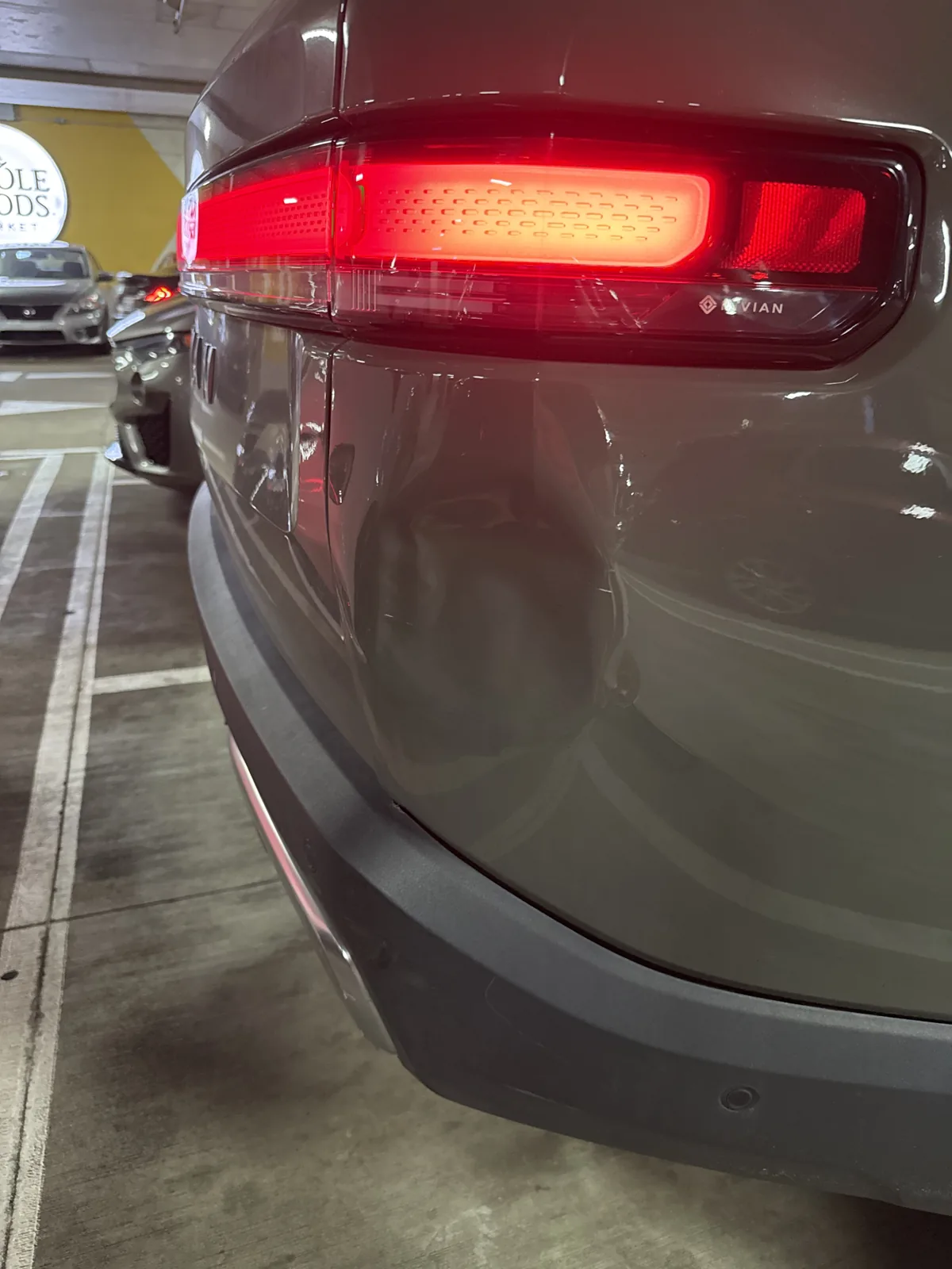 Dent on the rear quarter panel of a green Rivian R1S in a parking deck.