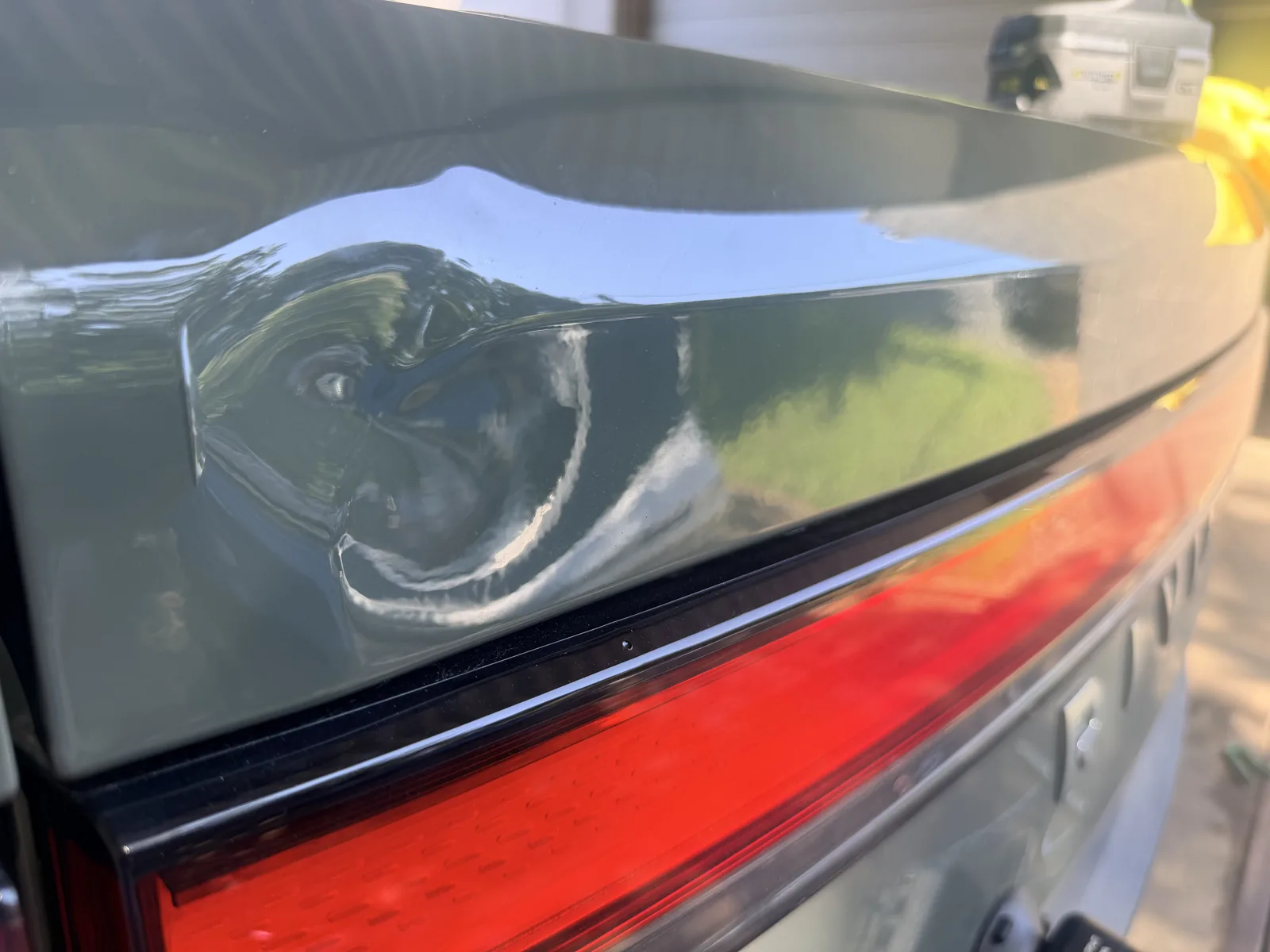 Large dent distorting the reflection on the tailgate of a forest green Rivian R1T.